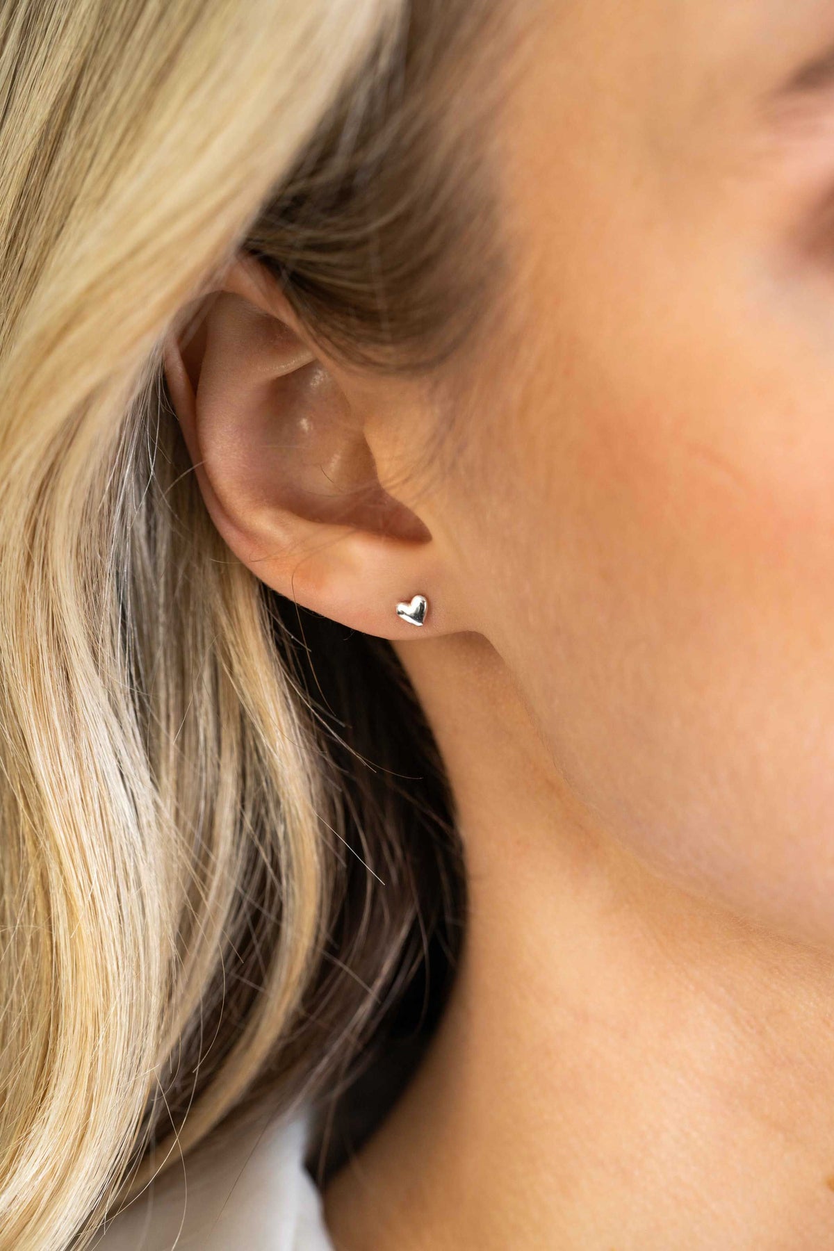 Close-up van het oor van een persoon met steil blond haar, die elegante Zinzi Oorbellen Zilver Zio2365 oorbellen draagt. De achtergrond is onscherp, waardoor het glanzende zilveren ontwerp en de kenmerkende stijl van het merk worden benadrukt.