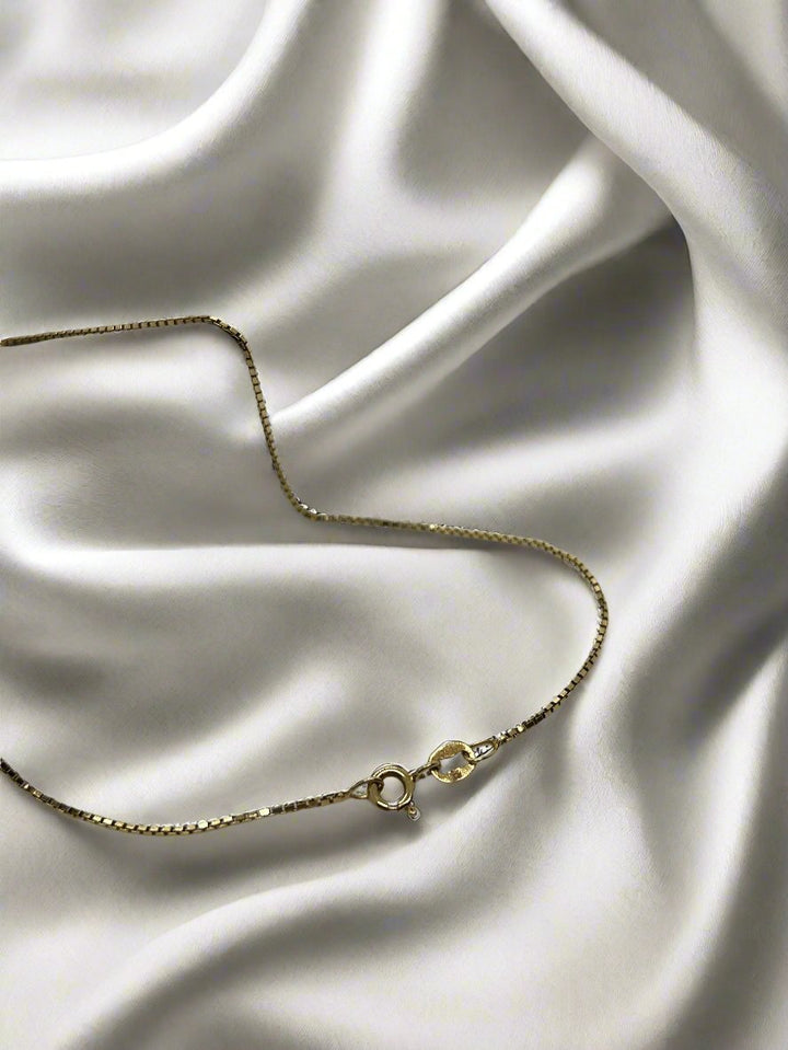 Het vintage gouden collier 45cm 14K Venetiaans van Juwelier van der Kooij, weegt 3,2 gram, is elegant uitgevoerd op gladde ivoorkleurige zijde, waarbij de delicate gloed prachtig contrasteert met de luxueuze stof.