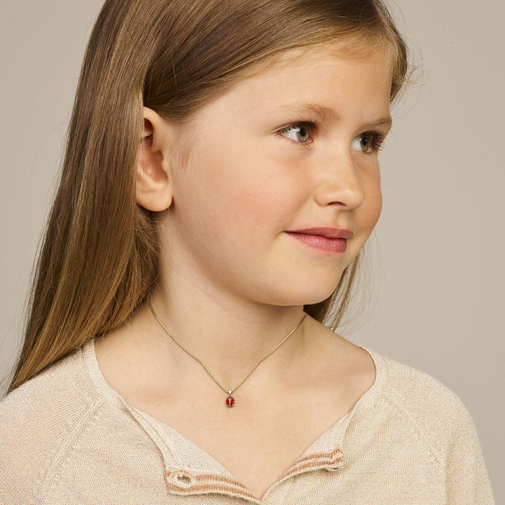 Een jong meisje met lang lichtbruin haar draagt een beige topje en het Van der Kooij Collectie hanger lieveheersbeestje 14K geelgoud collier. Ze glimlacht zachtjes terwijl ze iets naar rechts kijkt tegen een effen achtergrond.