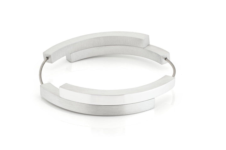 De Armband Vier bogen mat|glans A32 van CLIC Creations is een moderne, minimalistische armband met overlappende zilveren bogen die met elkaar verbonden zijn door een dunne draad en heeft een magnetische sluiting. Dit geometrische stuk is handgemaakt in Nederland en wordt tentoongesteld tegen een effen witte achtergrond.
