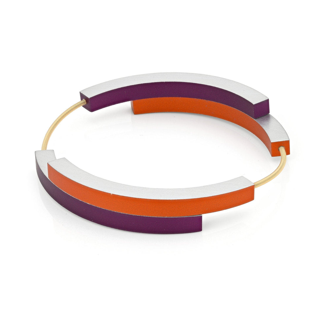 De Armband Vier bogen Oranje Paars AG32OP van CLIC Creations is een moderne, ronde armband handgemaakt in Nederland, met mat zilveren, oranje en paarse bogen verbonden door een slanke gouden band in een geometrisch ontwerp.