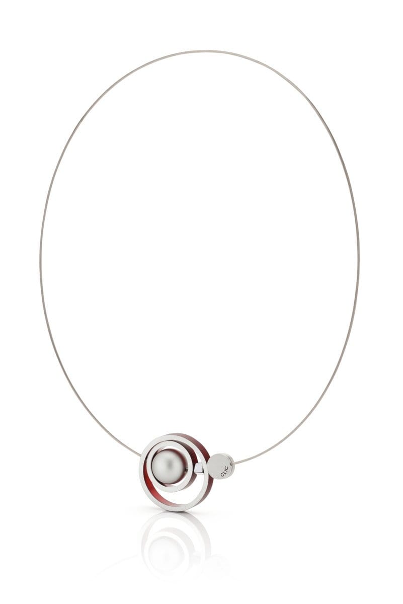 De Collier Ringen in elkaar Rood C187R van CLIC Creations is een minimalistische ketting die met de hand is gemaakt in Nederland, met een slanke ronde draad met een hanger van een bolvormige zilveren kraal en twee concentrische ringen, een rode en een zilveren. Het wordt elegant gepresenteerd tegen een effen witte achtergrond.