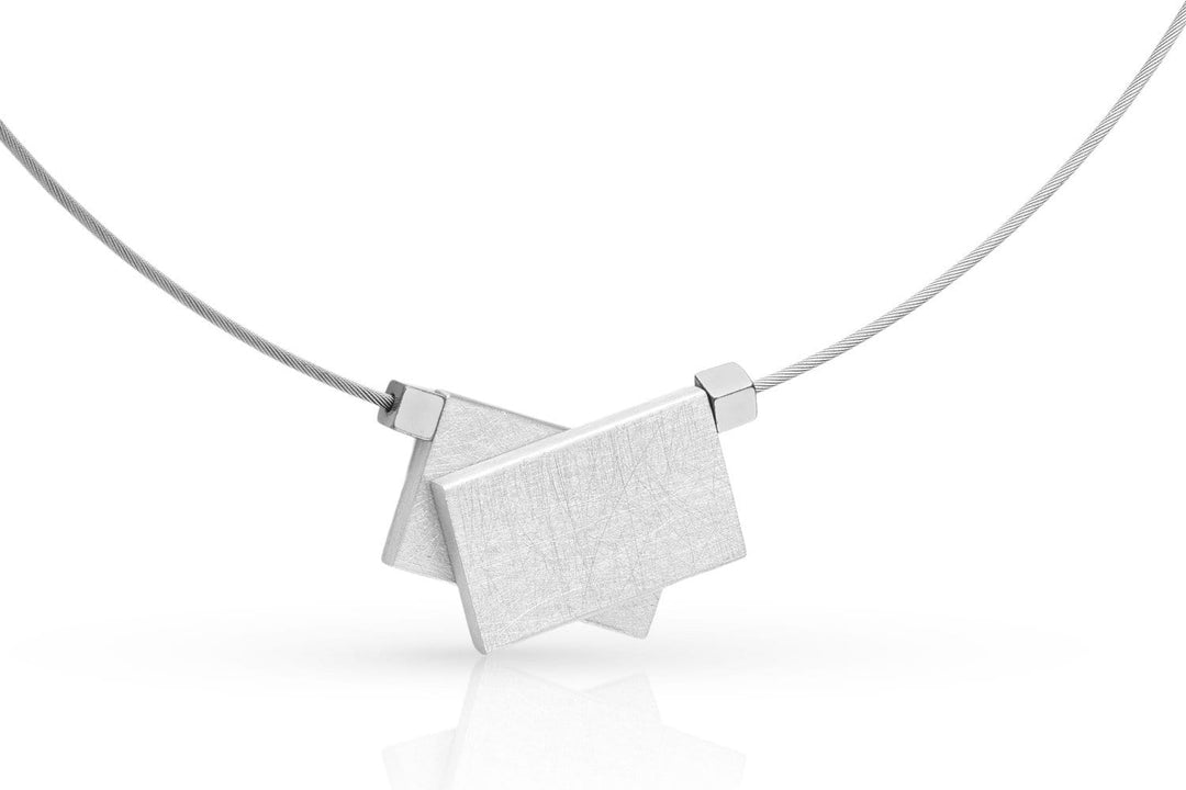 De CLIC Creations Collier gekruiste rechthoeken & hematiet C233 is een minimalistische zilveren ketting met twee overlappende geborstelde rechthoekige hangers aan een dunne draadketting, versterkt door geometrisch ontwerp en hematietstenen voor subtiele elegantie.