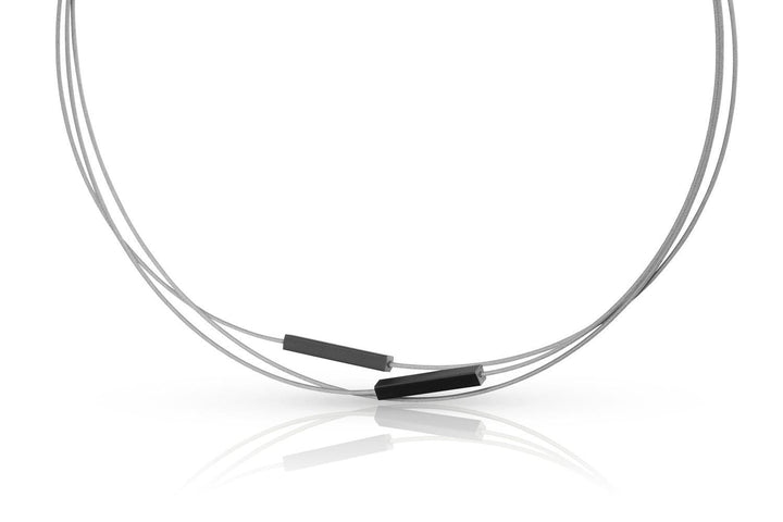 De Collier Staafjes Zwart C243Z van CLIC Creations is een minimalistisch stuk met drie dunne draden met twee kleine rechthoekige zwarte kralen tegen een witte achtergrond. De draden, elegant gebogen voor beweging, zijn versterkt met een edelstalen bajonetsluiting.