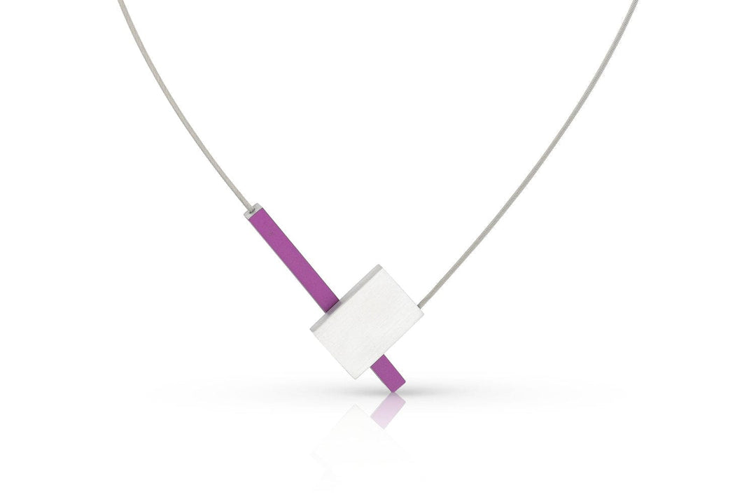 De Collier V-vorm met staafje C261P van CLIC Creations is een moderne ketting met een dunne, zilveren draad en minimalistische hanger met een horizontale witte rechthoek die een verticale paarse balk kruist. Het is handgemaakt in Nederland en heeft een magnetische sluiting tegen een witte achtergrond.