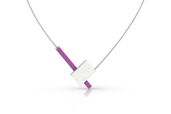 De Collier V-vorm met staafje C261P van CLIC Creations is een moderne ketting met een dunne, zilveren draad en minimalistische hanger met een horizontale witte rechthoek die een verticale paarse balk kruist. Het is handgemaakt in Nederland en heeft een magnetische sluiting tegen een witte achtergrond.