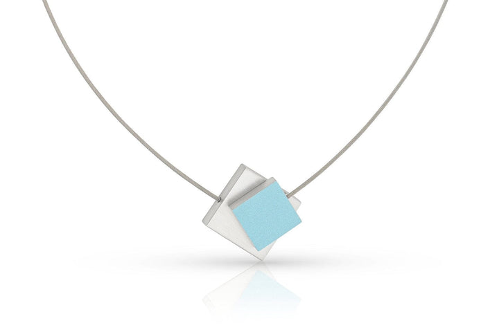 Het Collier Vierkant met gekleurd vierkant C263B van CLIC Creations is een minimalistisch sieraad met een dunne draad en een geometrische hanger van overlappende zilveren en lichtblauwe vierkanten, wat een moderne, stijlvolle look creëert.