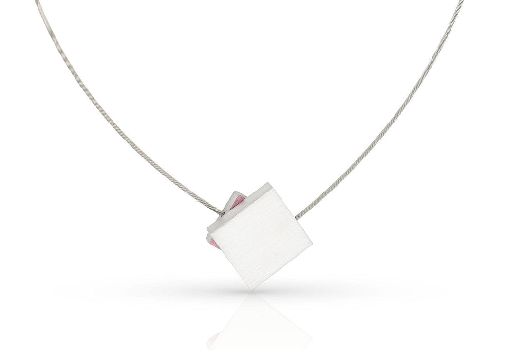 De Collier Vierkant met gekleurd vierkant C263R van CLIC Creations heeft een strak, minimalistisch ontwerp met een dunne draad en een geometrische hanger versierd met roze vierkanten, elegant geplaatst tegen een witte achtergrond.
