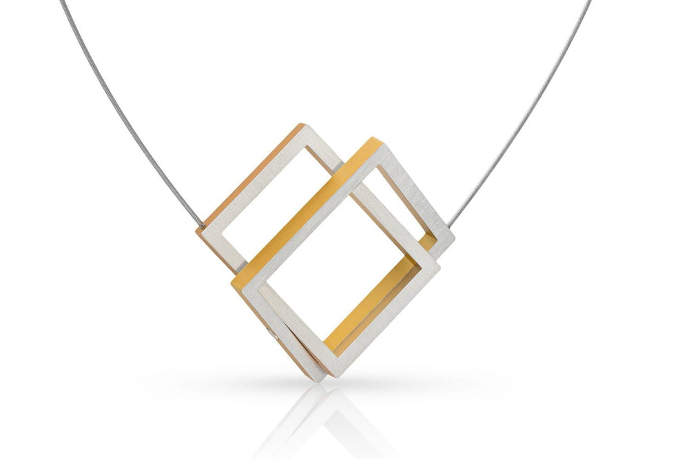 De Collier Twee rechthoeken in elkaar Goud|Geel C30G van CLIC Creations heeft overlappende zilveren en gouden vierkante frames aan een delicate ketting, wat een minimalistisch geometrisch ontwerp biedt. Handgemaakt in Nederland voor een moderne, elegante uitstraling.