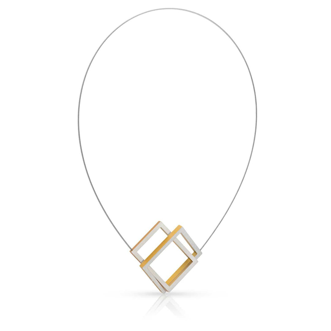 De Collier Twee rechthoeken in elkaar Goud|Geel C30G van CLIC Creations is een geometrische ketting gemaakt in Nederland, bestaande uit twee in elkaar grijpende rechthoekige frames, één van zilver en één van goud, op een dunne gebogen draad, wat een eenvoudige maar toch eigentijdse esthetiek oplevert.