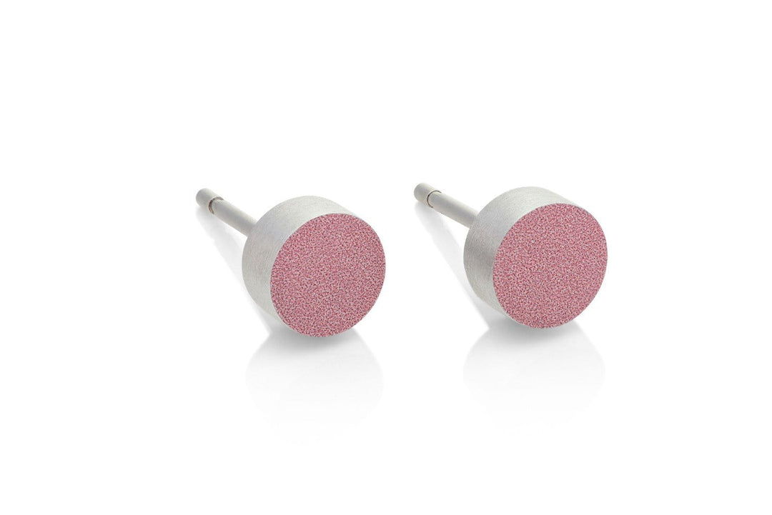 De Oorsteker Klein rond Roze O36RO van CLIC Creations heeft twee roze, cilindrische elementen met metalen schachten. Hun ontwerp roept ambachtelijke ambacht op, uit elkaar geplaatst op een reflecterend wit oppervlak en lichtjes naar links gekanteld.