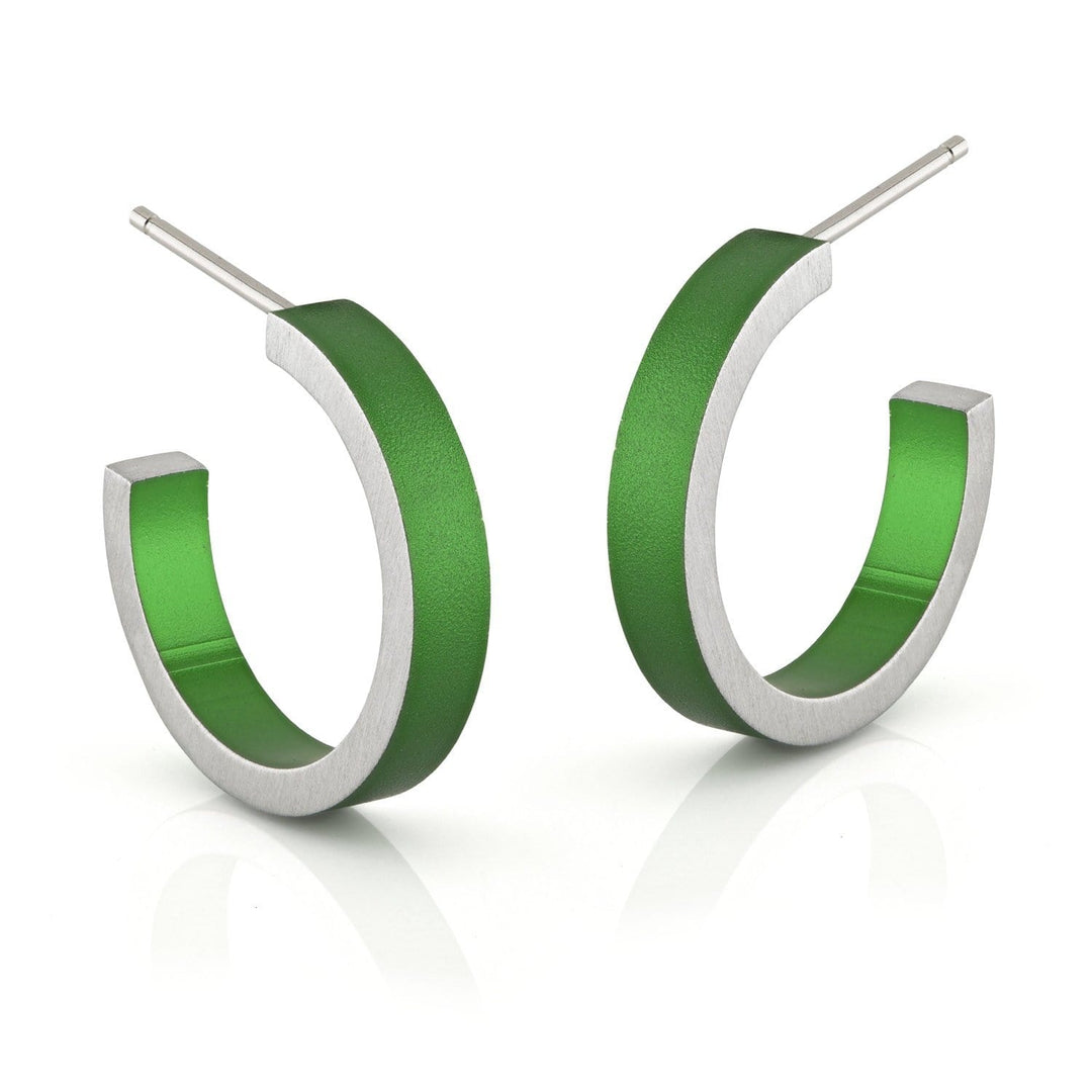 De Creolen Ronde ringetjes Groen O51GR van CLIC Creations zijn moderne creolen gemaakt van hypoallergeen aluminium. Ze hebben een matte zilveren buitenkant en een glanzende groene binnenkant met een hol ontwerp en gebogen staafjes, afgebeeld op een reflecterend wit oppervlak.
