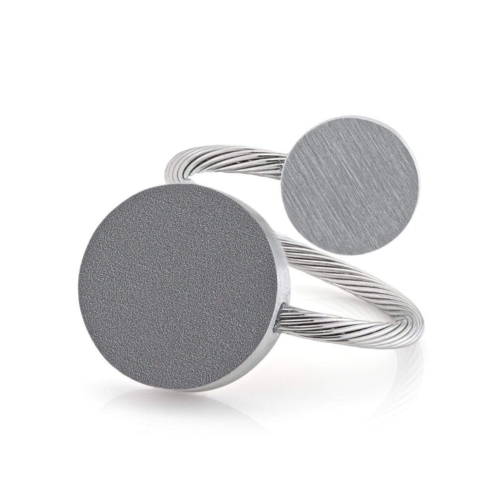 De CLIC Creations Ring Twee ronde vormen Grijs R5AG heeft een gedraaide metalen band met twee getextureerde schijven van verschillende groottes, geplaatst tegen een stijlvolle witte achtergrond. Het verstelbare ontwerp biedt moderne, minimalistische veelzijdigheid voor elke maat.