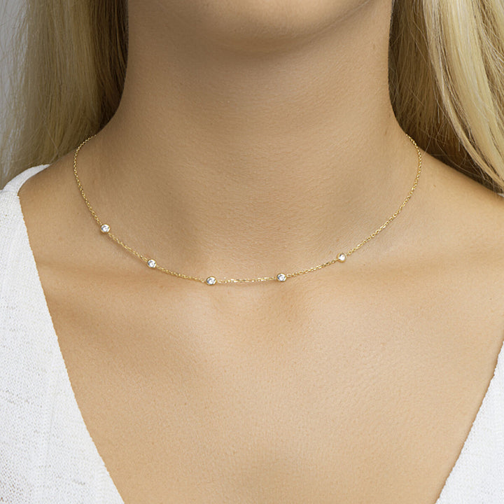 Een close-up van de nek van een vrouw met een Van der Kooij Collectie gouden dames ketting met zirkonia, zilver verguld (geel), gecombineerd met een witte top.