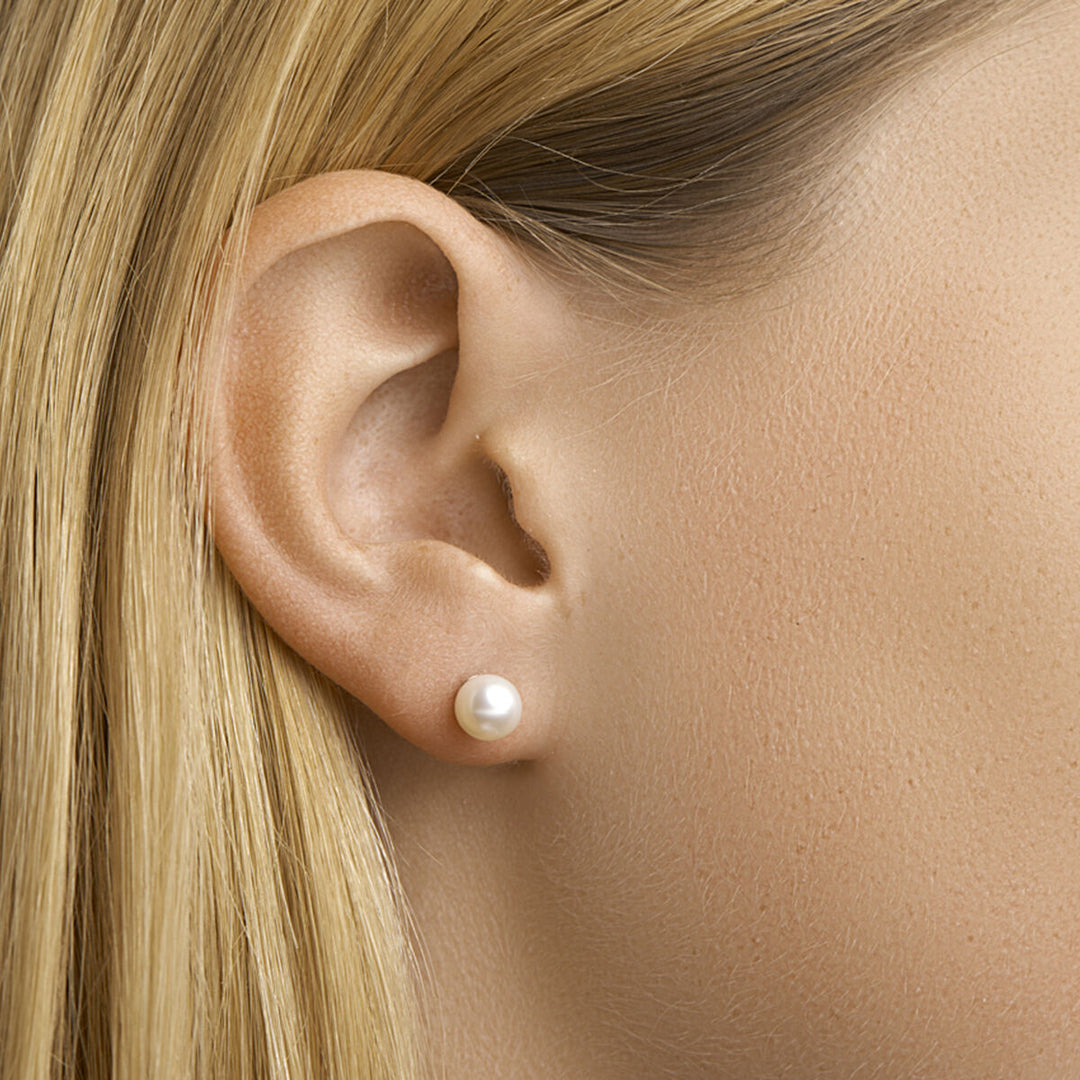 Close-up van een lichtgekleurd persoon met steil blond haar, gekleed in een Van der Kooij Collectie oorknoppen van parelmoer in 14K geelgoud. De achtergrond is neutraal.