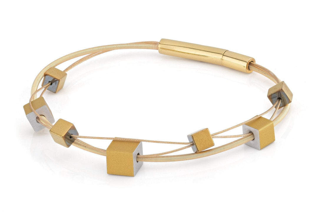 De Armband speelse kubusjes goud A257G van CLIC Creations heeft een strakke gouden band met kleurrijke kubieke metalen kralen. Het is minimalistisch, hypoallergeen en bevat een cilindrische bajonetsluiting voor sluiting, geschikt voor de gevoelige huid.