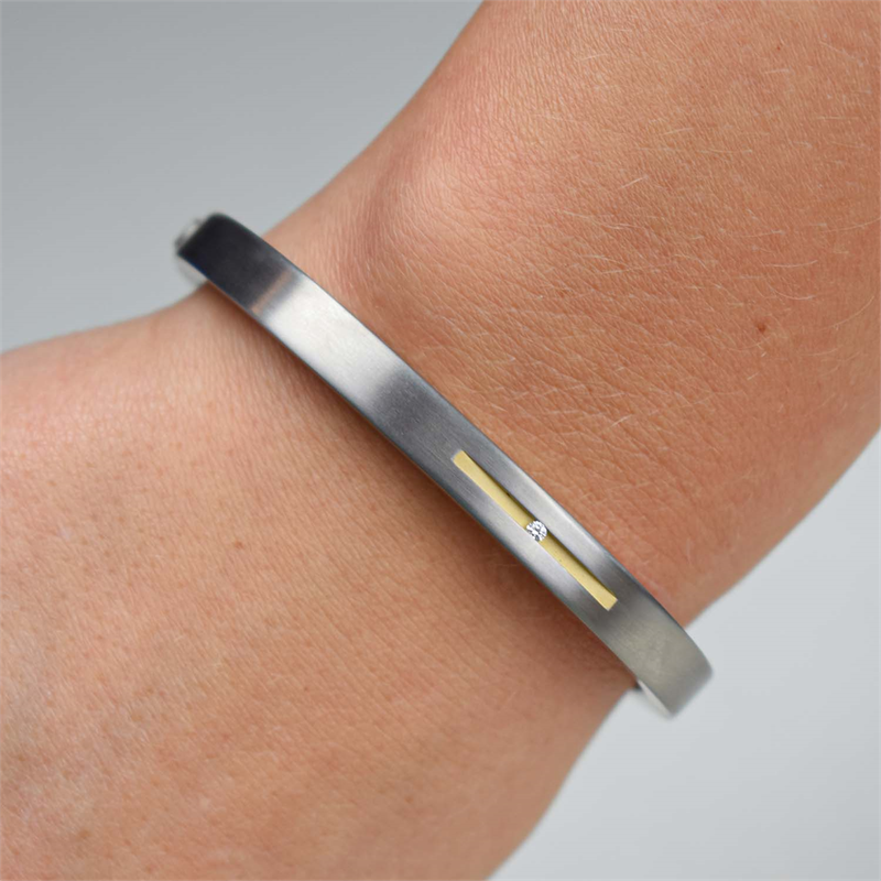Een close-up van een pols die de Boccia Titanium Armb. Sp. Bicolor 0304-01, een moderne, minimalistische armband van Boccia met een slanke tweekleurige afwerking, dunne gouden lijn en kleine ingebedde diamant.