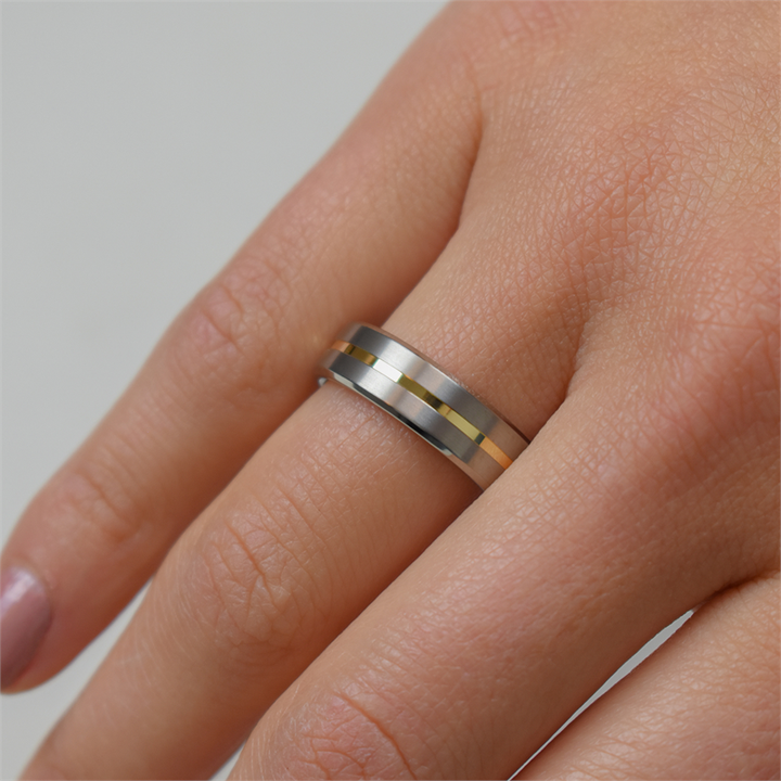 Een close-up van een hand met de Boccia Titanium Ring Bicolor 0101-03 van Boccia, met gouden en zwarte strepen. De korte nagels met lichtroze nagellak accentueren het goudkleurige accent van de ring.
