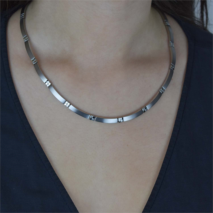 Een persoon draagt een donker topje met V-hals en een Boccia Titanium Collier 0831-01, een strakke Boccia-ketting met kleine rechthoekige accenten, gemaakt van duurzame materialen, om de nek.