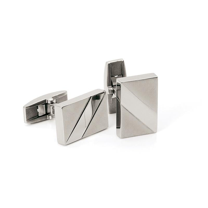 De Boccia Titanium Manchetknopen 0603-01 van Boccia zijn rechthoekige, gematteerde zilverkleurige manchetknopen met een minimalistisch geometrisch ontwerp, waarbij diagonale lijnen subtiele driehoekige patronen vormen op een onberispelijk witte achtergrond.
