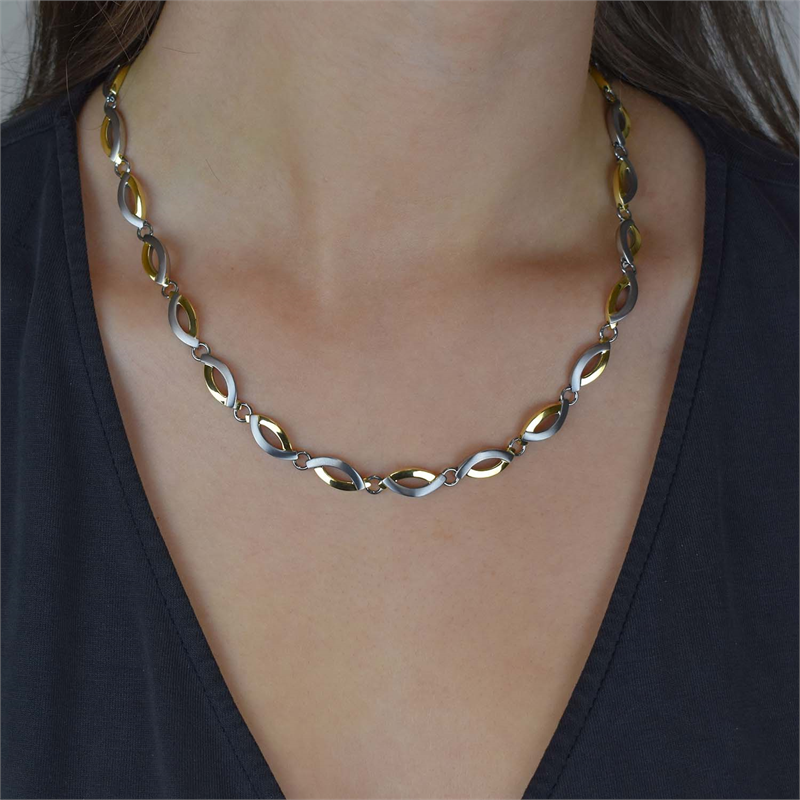 Een persoon in een donkere top met V-hals draagt de Boccia Titanium Collier Bicolor 0876-02, met in elkaar grijpende bladaccenten van goud en zilver. De afbeelding benadrukt de goudkleurige accenten en de bovenkant van de borst. Merk: Boccia.