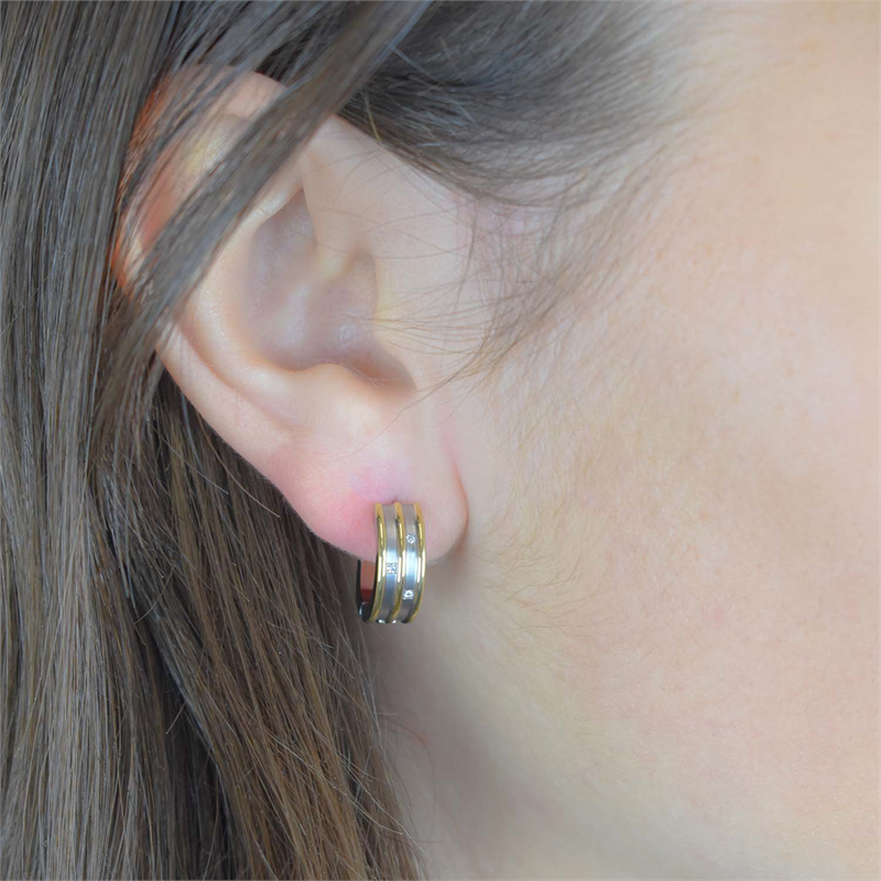 Een close-up van het oor van een persoon met lang bruin haar, die een kleine, dikke Boccia Titanium Oorringen Bicolor dia 6/0.03 - 05047-03 creool draagt in stijlvol zilver en goud van Boccia.