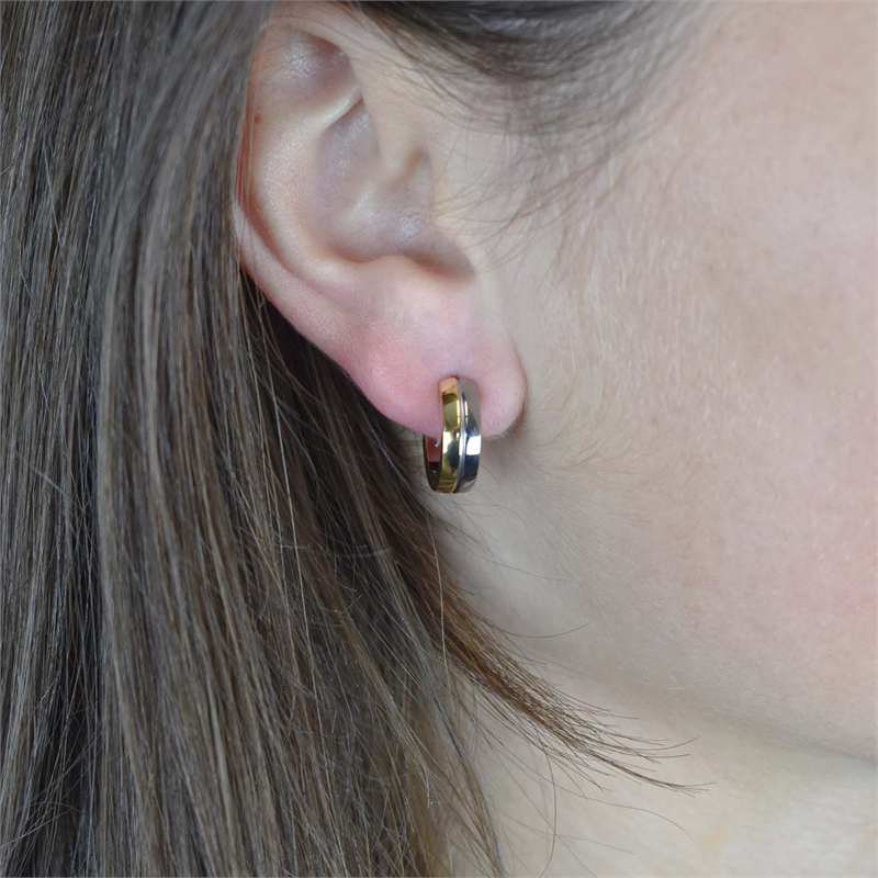 Close-up van het oor van een persoon met steil bruin haar, die een Boccia Titanium Oorring Bicolor 0539-07 draagt. De kleine, goud-zilveren oorbel van Boccia steekt af tegen de zacht wazige achtergrond en benadrukt het elegante ontwerp.