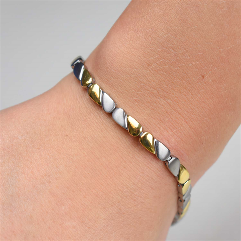 Close-up van een pols met de Boccia Titanium Armband Bicolor 03016-02 van Boccia, met gouden en zilveren hartvormige schakels, tegen een lichte achtergrond.