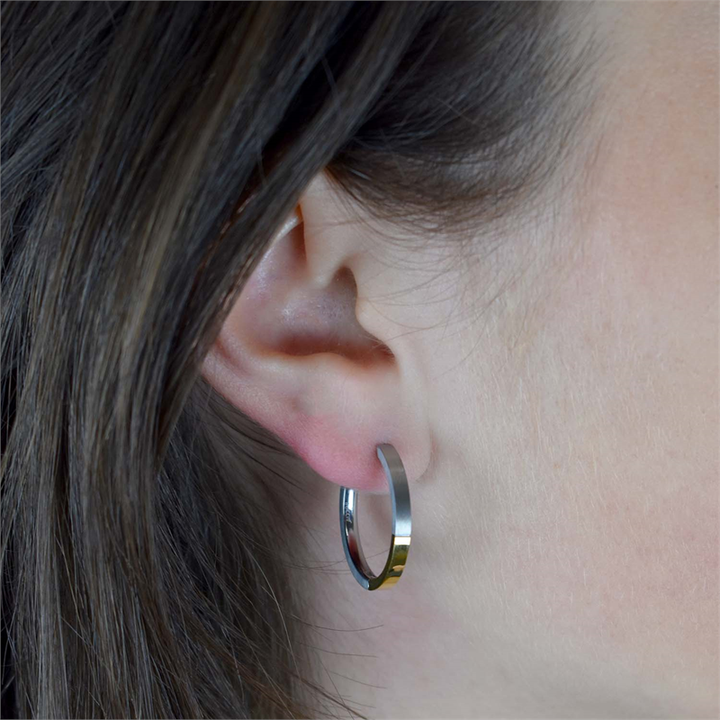 Close-up van het oor van een persoon met steil bruin haar, die een Boccia Titanium Oorring Bicolor 0517-02 draagt. De middelgrote, glanzende oorringen van Boccia hebben een gladde afwerking die goed afsteekt tegen de huid en het haar.