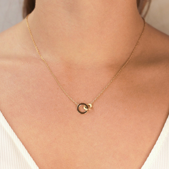 Een close-up van een vrouw die de Boccia Titanium Collier gp 08033-03, met twee in elkaar grijpende cirkels, tegen haar blote nek en sleutelbeen draagt. Ze is gekleed in een witte top met V-hals en textuur.