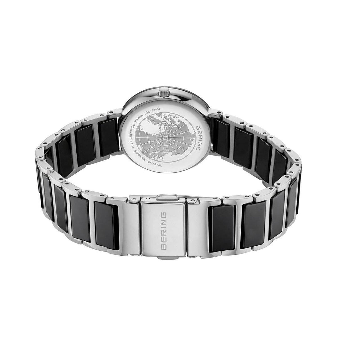 Het Bering dames horloge zwarte wijzerplaat - 11429-702 is een zilverkleurig dameshorloge met een zwarte keramische inlegband, een gegraveerde wereldkaart op de achterkant van de kast, duurzaam saffierglas en elegante details van Bering.