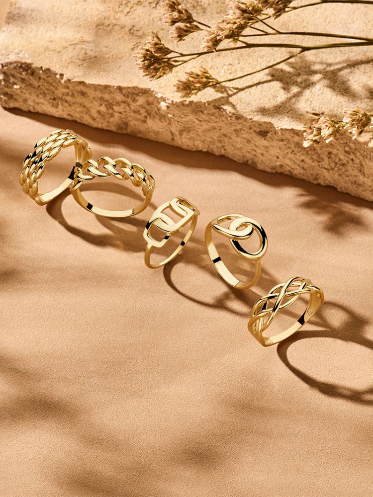 De Geelgouden Damesring van Excellent Jewelry, eenvoudig maar elegant in 14 karaat goud, ligt op een beige ondergrond met zachte schaduwen van dorre planten-de perfecte tijdloze ring voor elke gelegenheid.
