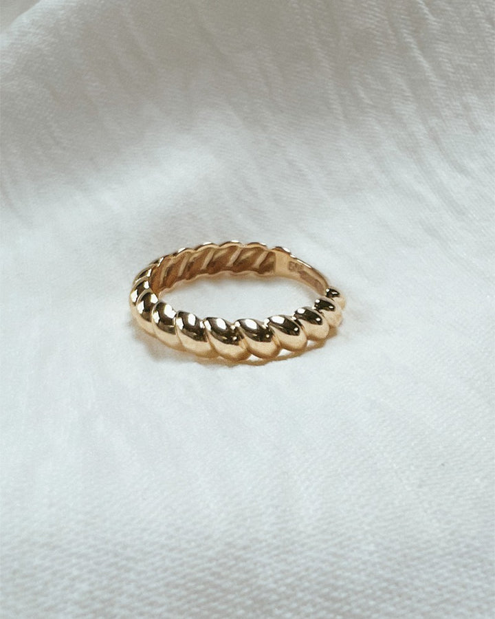 De Geelgouden Gedraaide Bandring van Excellent Jewelry (14kt, 4,3 mm breed, 1,8 g) ligt op zacht wit textiel met subtiele structuur.