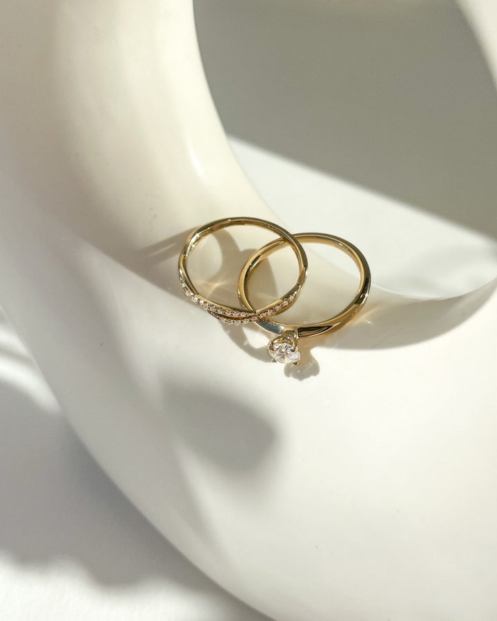 Twee gouden ringen van Excellent Jewelry rusten op een glad wit oppervlak; de ene is de "Elegante Gouden Solitair Ring met 0,40 crt Briljant - Subtiele Luxe voor Dames" en de andere heeft kleine diamanten langs de band.