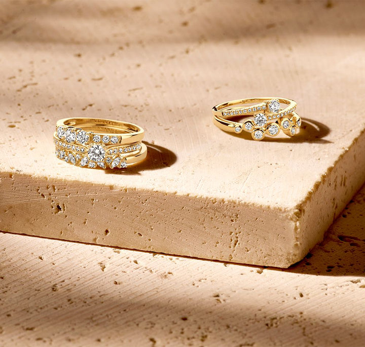 De Elegante Geelgouden Ring met Zirkonia's in Golvend Design van Excellent Jewelry schittert op een beige stenen ondergrond, waarbij 14 karaat goud en zirkonia's stralen in het zachte zonlicht.