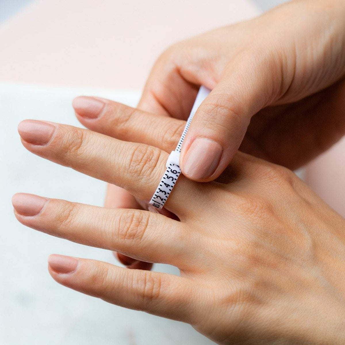 Finger mit einem Ringmaß, das die Ringgröße bestimmt, auf einem hellen Untergrund