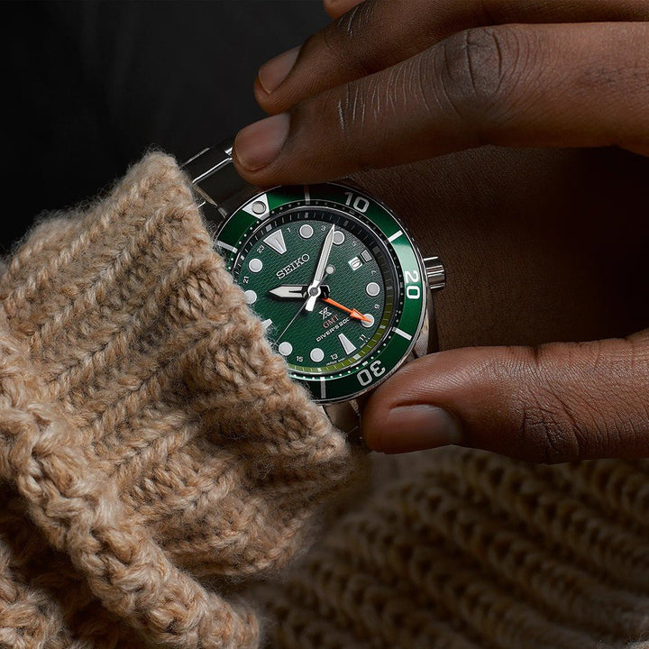 Met een gebreide beige trui aan, past iemand zijn Seiko Prospex heren horloge SFK003J1 aan. Dit horloge heeft een solar uurwerk met een groene wijzerplaat, witte uurmarkeringen en een draaibare lunette met minutenmarkeringen.