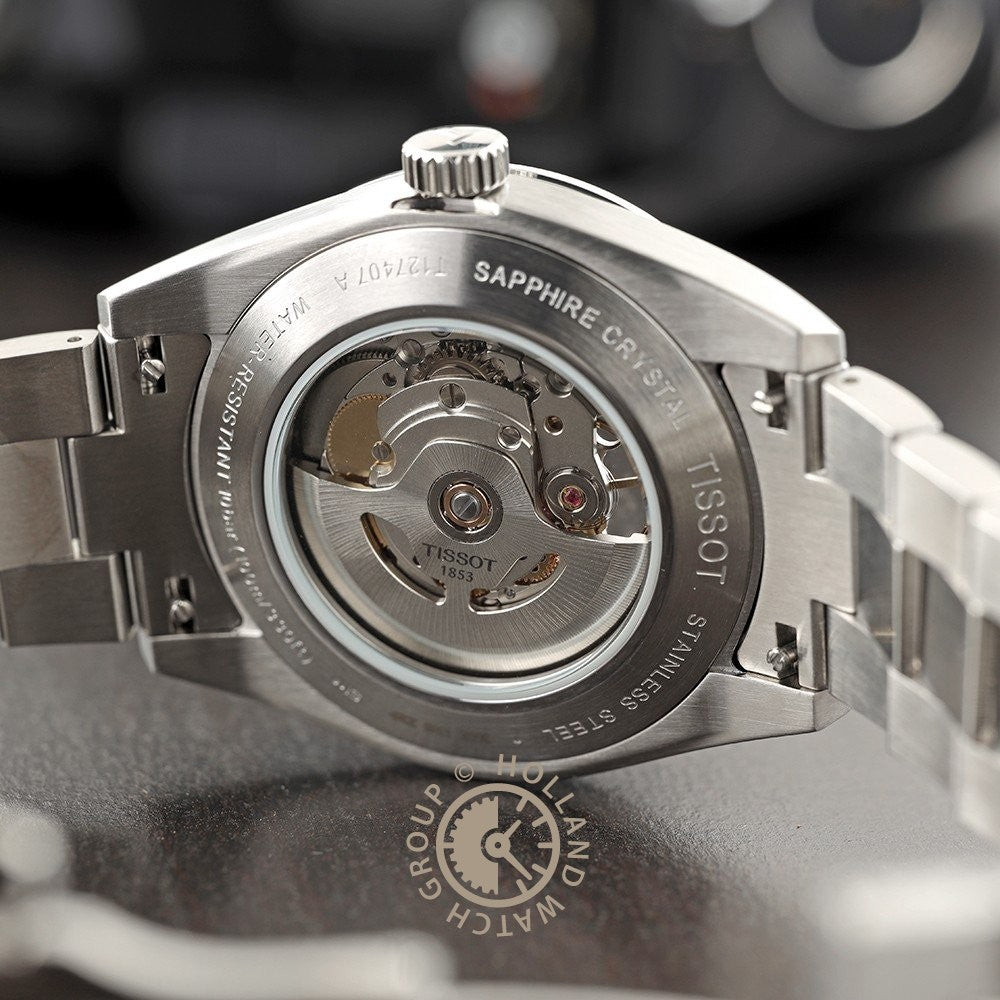 Close-up van de transparante achterkant van de Tissot Gentleman Powermatic 80 Open Heart kast, waarop het automatische uurwerk en de gegraveerde details op de metalen rand te zien zijn, elegant geplaatst op een donker oppervlak.