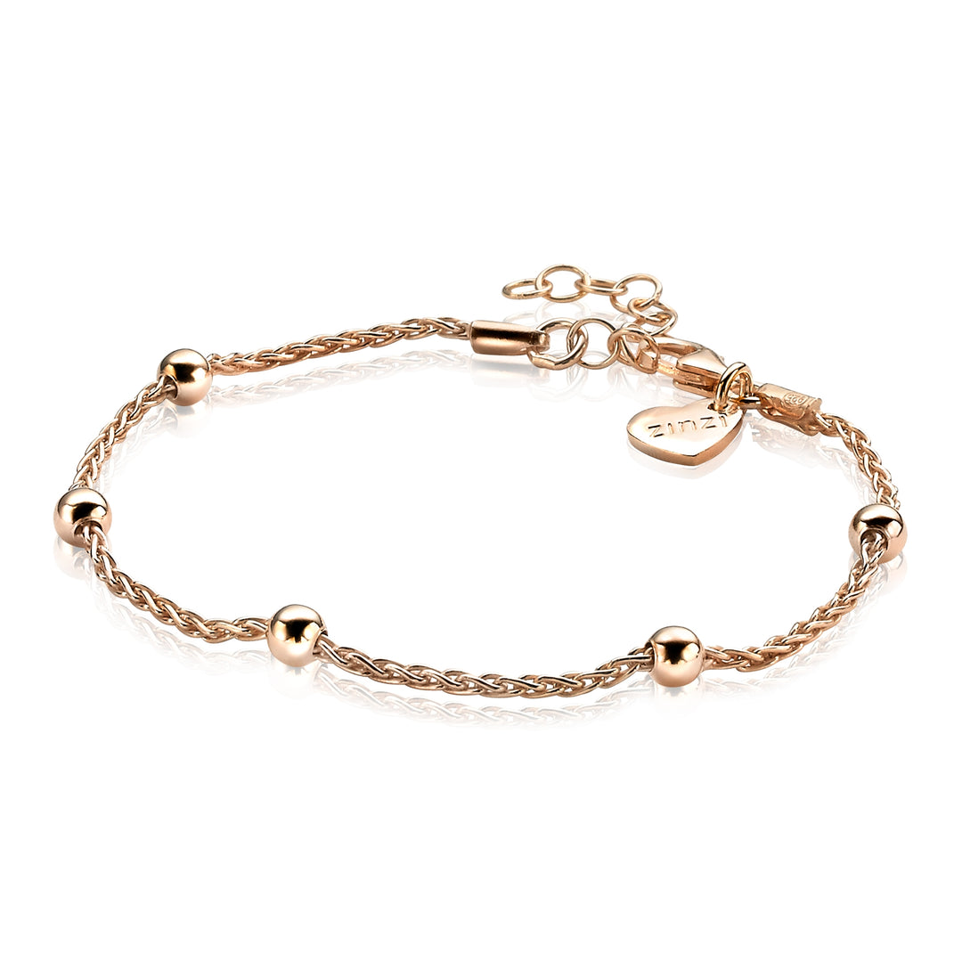 De Zinzi Armband Gold Plated Zia1128 R is een delicate rosé armband met een gedraaide ketting, versierd met kleine gouden bolletjes. Het heeft een verstelbare sluiting en een hartvormige bedel met de merknaam Zinzi, tegen een witte achtergrond.